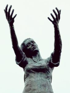 Frau mit sehnsuchtsvoll ausgestreckten Armen. Sinnbild für starke Emotionen, die sich im systemischen Erstgespräch zeigen können. Warten am Ufer – Bronzestatue in Rosses Point, Irland.